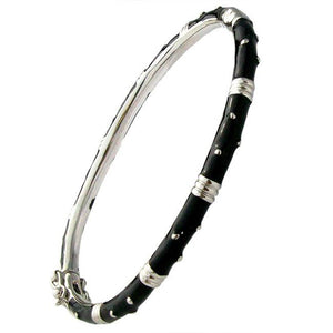 The zirconmania Bracelet Thin Gold tone Enamel Bangle 501B5339 features a slender, bamboo-inspired design with gold and black enamel segments and metallic accents wrapping around the bracelet.