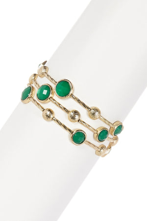 The zirconmania Bracelet Multi-Wire Gold and Beads Bangle 22B0241A features three overlapping gold bands with round green stones and textured gold discs, displayed on a white cylinder—an elegant accessory for any occasion.