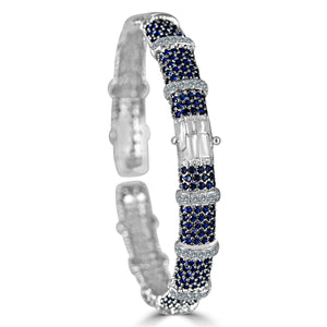The zirconmania Bracelet Face-off line Stations wide fine Cubic Zirconia Set Hinged Bangle 698B100 features silver with rows of blue gemstones, clear diamonds, and a central rectangular cluster of sparkling zirconite stones. Shown on white background.