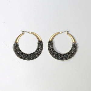 A pair of zirconmania Textured Satin Bezel Alloy Setting Hoop Earrings (661E581) with hinged saddle closure posts, featuring a gold Art-deco design and dark, glittery stone accents, shown on a plain white background.